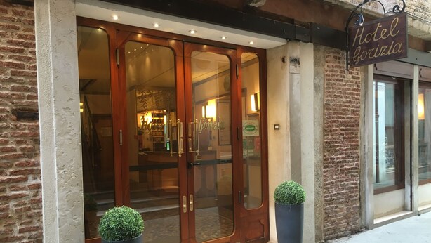 Entrada de hotel com porta de madeira, painéis de vidro e uma placa com a inscrição 'Hotel Gorizia'.