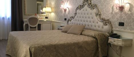 A hotel room with a large bed, a desk, a chair, a mirror, and a wall-mounted phone.