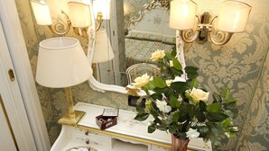 Uma toucador com espelho, uma luminária, um vaso com flores, uma bandeja com um bule, xícaras e materiais de escrita.