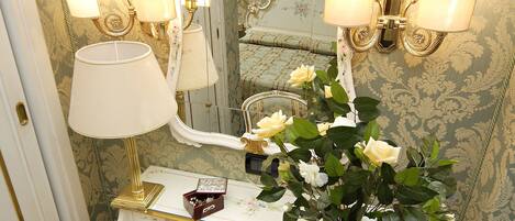 A vanity with a mirror, a lamp, a vase with flowers, a tray with a teapot, cups, and writing materials.