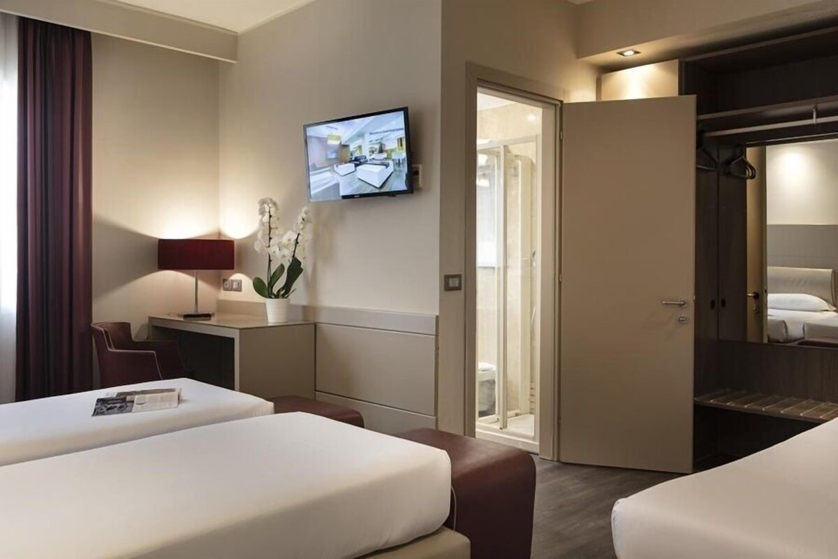 A hotel room with two beds, a desk with a lamp, a TV, and a sliding door to a bathroom.