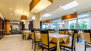Un comedor amplio con varias mesas y sillas, ventanas grandes y lámparas modernas.