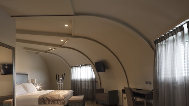 Un dormitorio moderno con techo curvo, una cama, un escritorio y una silla.