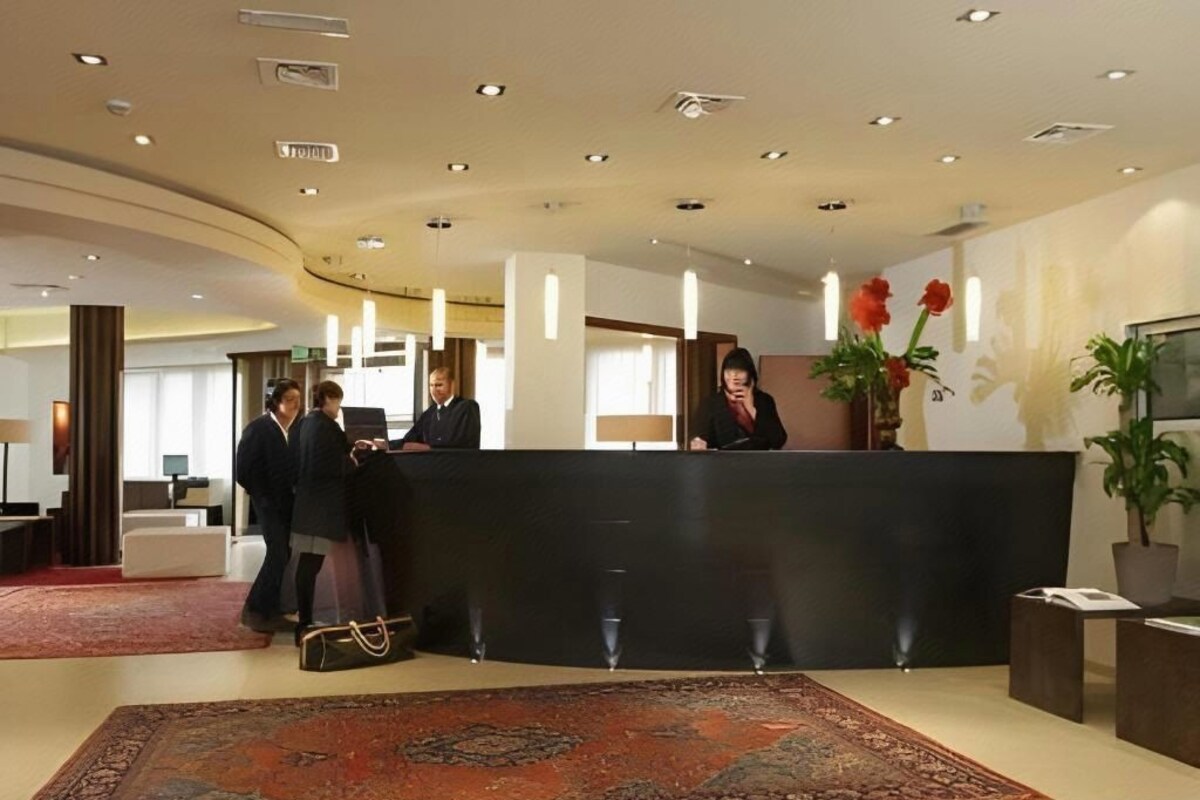 A reception area with a black reception desk, a large patterned rug, and a potted plant.