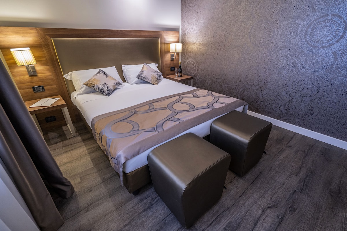 Un lit bien fait, avec une tête de lit, deux tables de chevet avec des lampes, un mur décoré d’un motif et un plancher en bois.