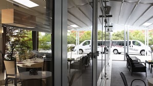 Un espacio al aire libre con mesas y sillas, una planta en maceta y vista de una camioneta blanca estacionada afuera.
