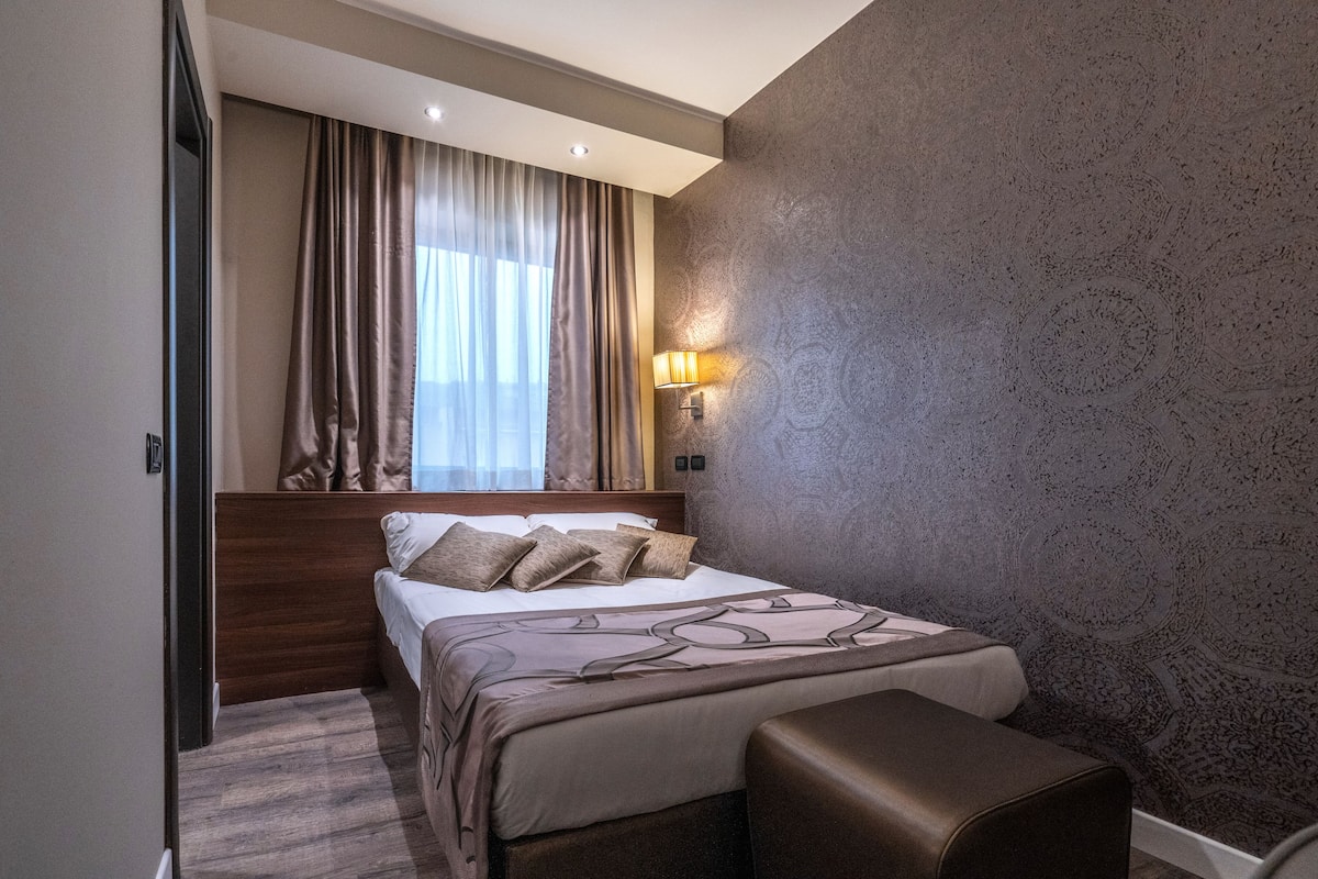 Une chambre d’hôtel avec un lit, une table de chevet, une lampe et un mur décoré d’un motif.