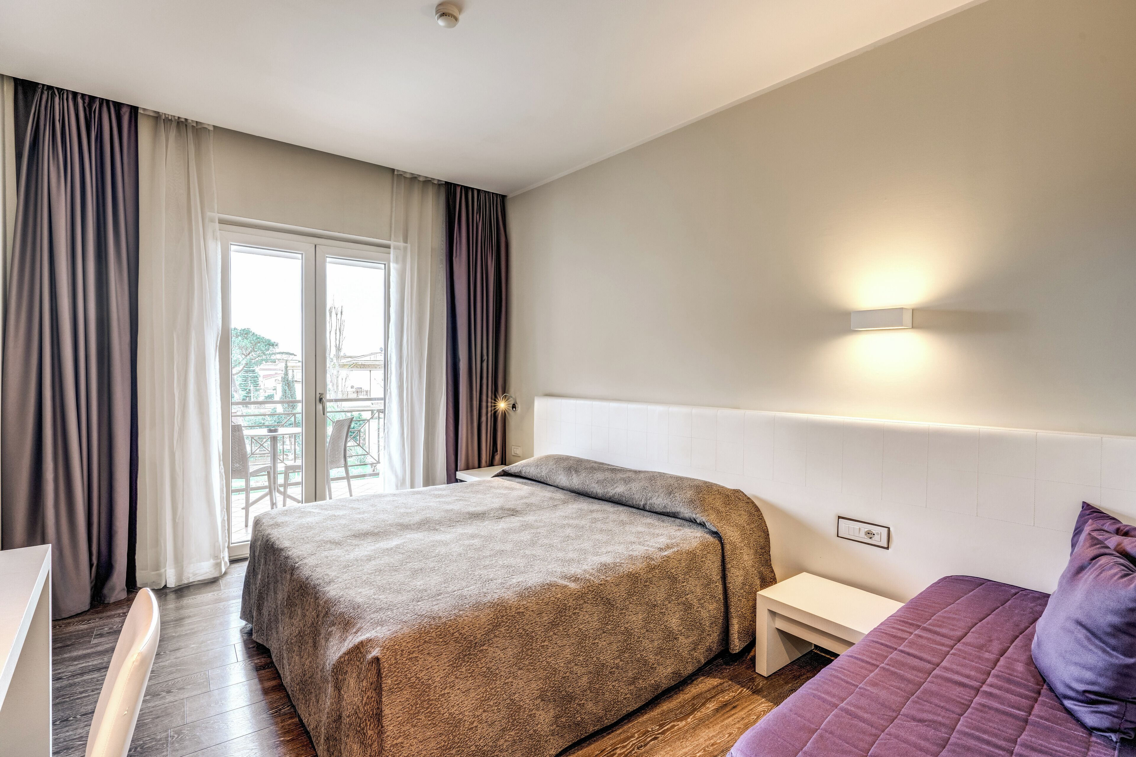 A hotel room with a large bed, a bedside table, a desk, and a window with curtains.
