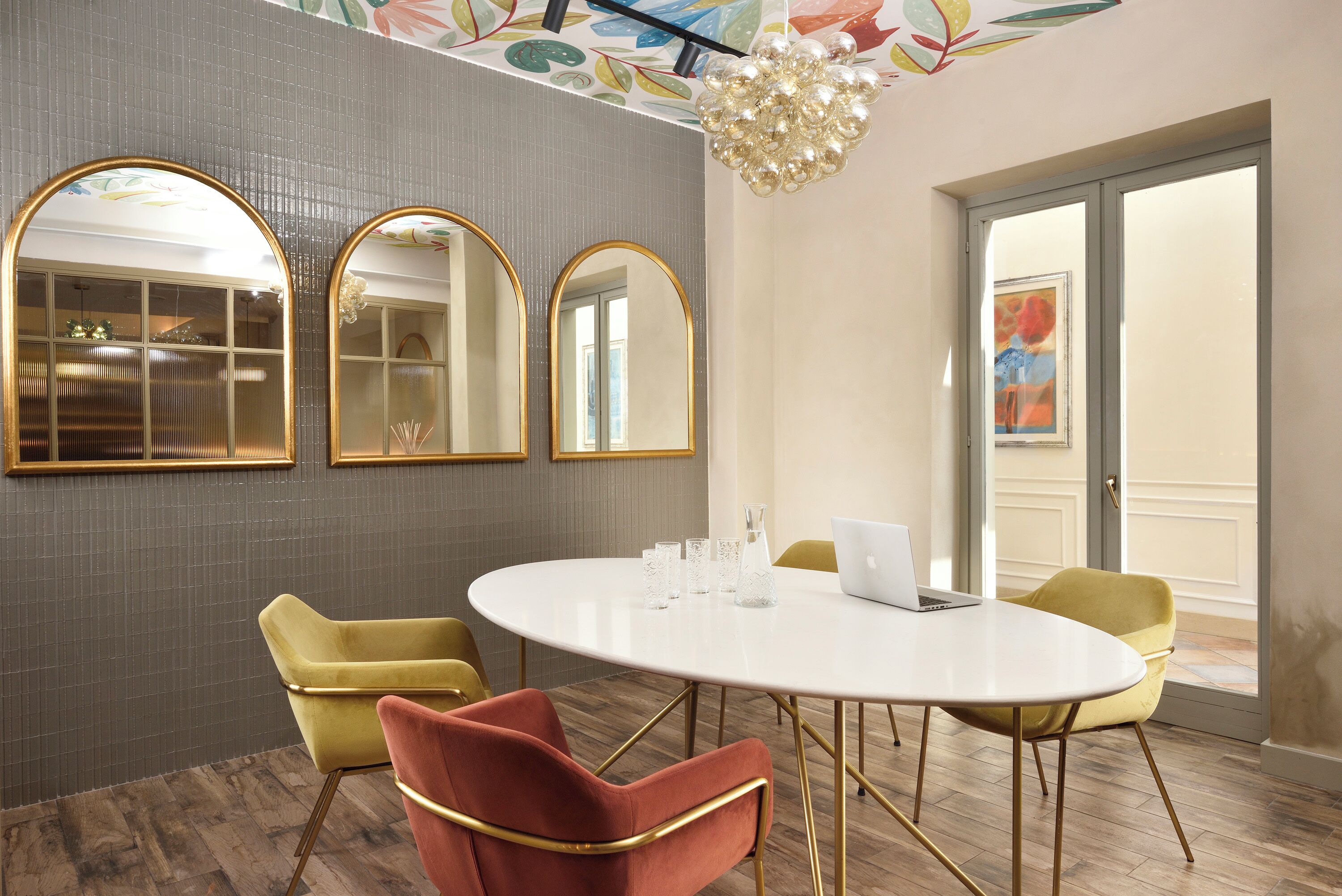 Une salle de conférence avec une table ronde, des chaises jaunes et rouges, trois miroirs et un ordinateur portable.