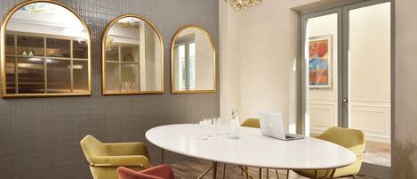 A conference room with a round table, yellow and red chairs, three mirrors, and a laptop.