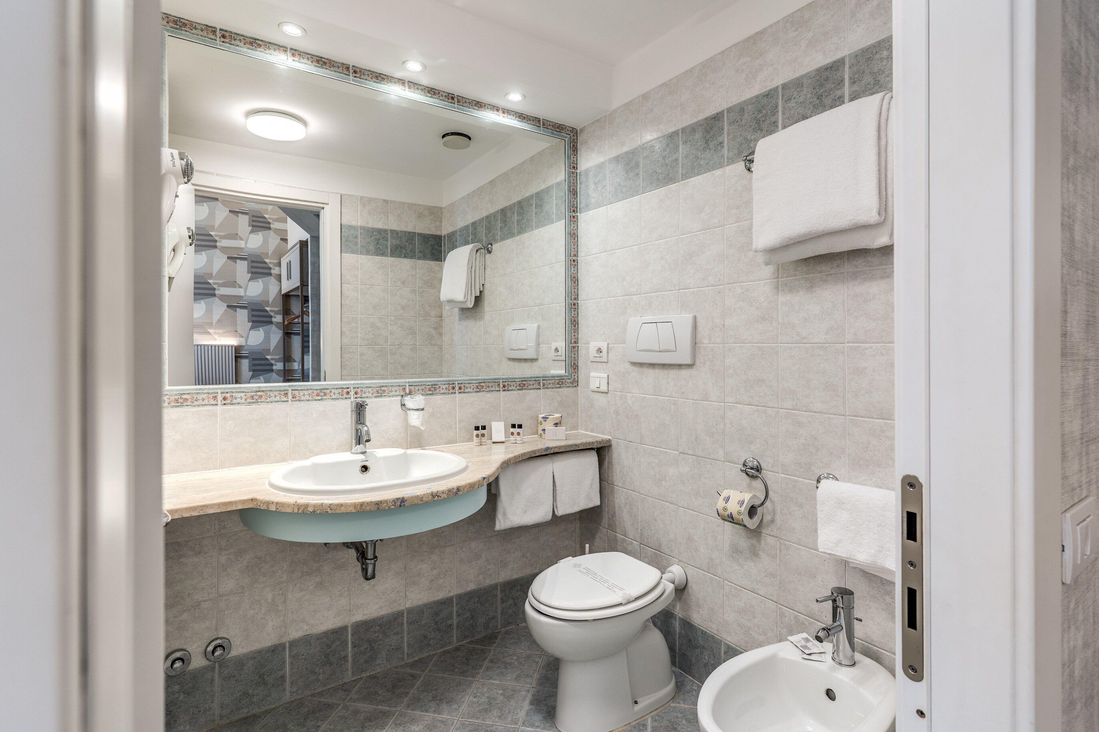 A modern bathroom with a sink, toilet, bidet, and a large mirror.