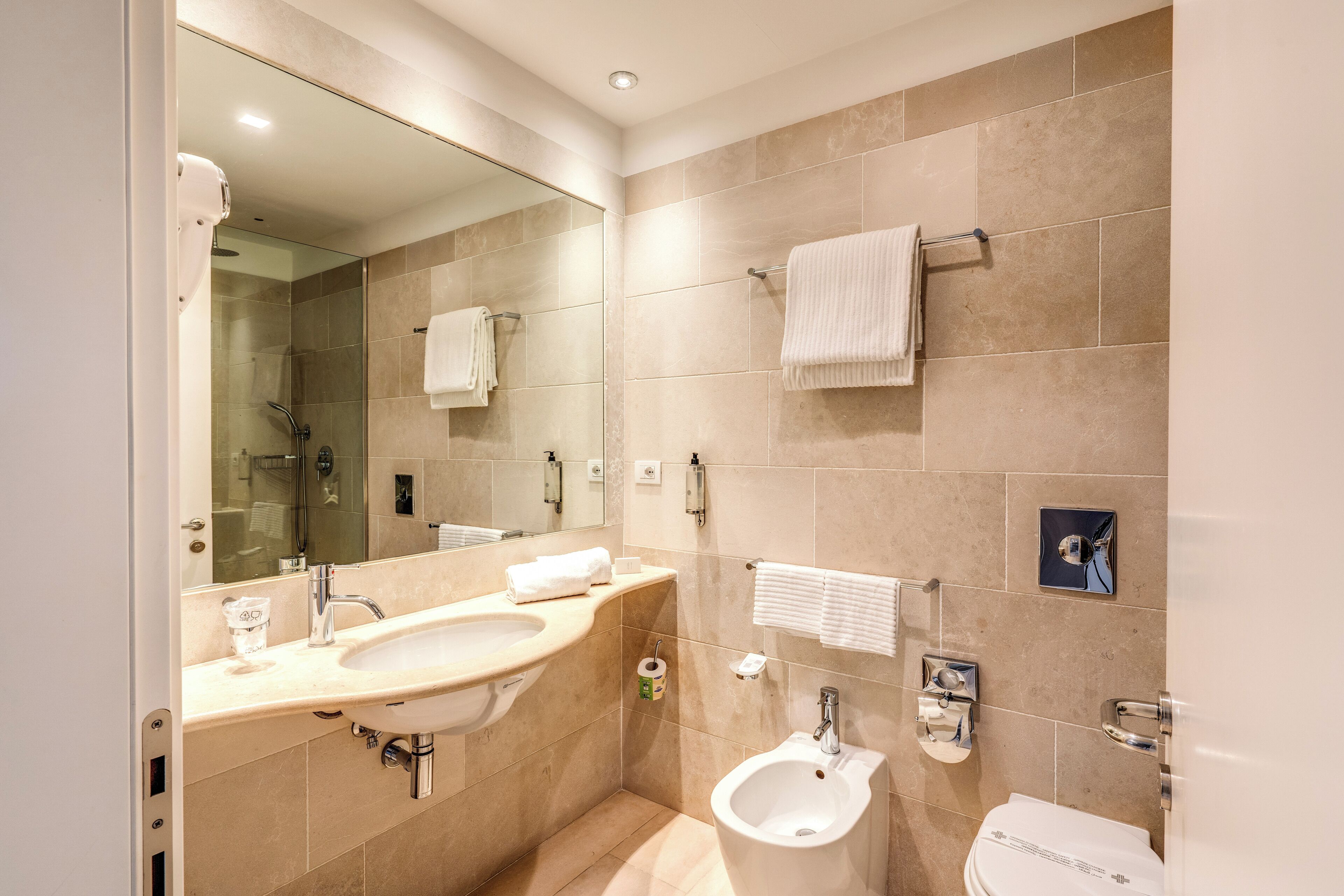 A modern bathroom with a sink, bidet, toilet, and a large mirror.