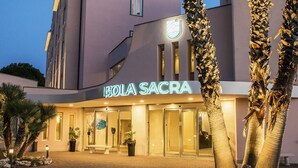 A hotel with a modern facade, a prominent sign reading "ISOLA SACRA," and palm trees in the foreground. - Hotel Isola Sacra Rome Airport (Fiumicino)