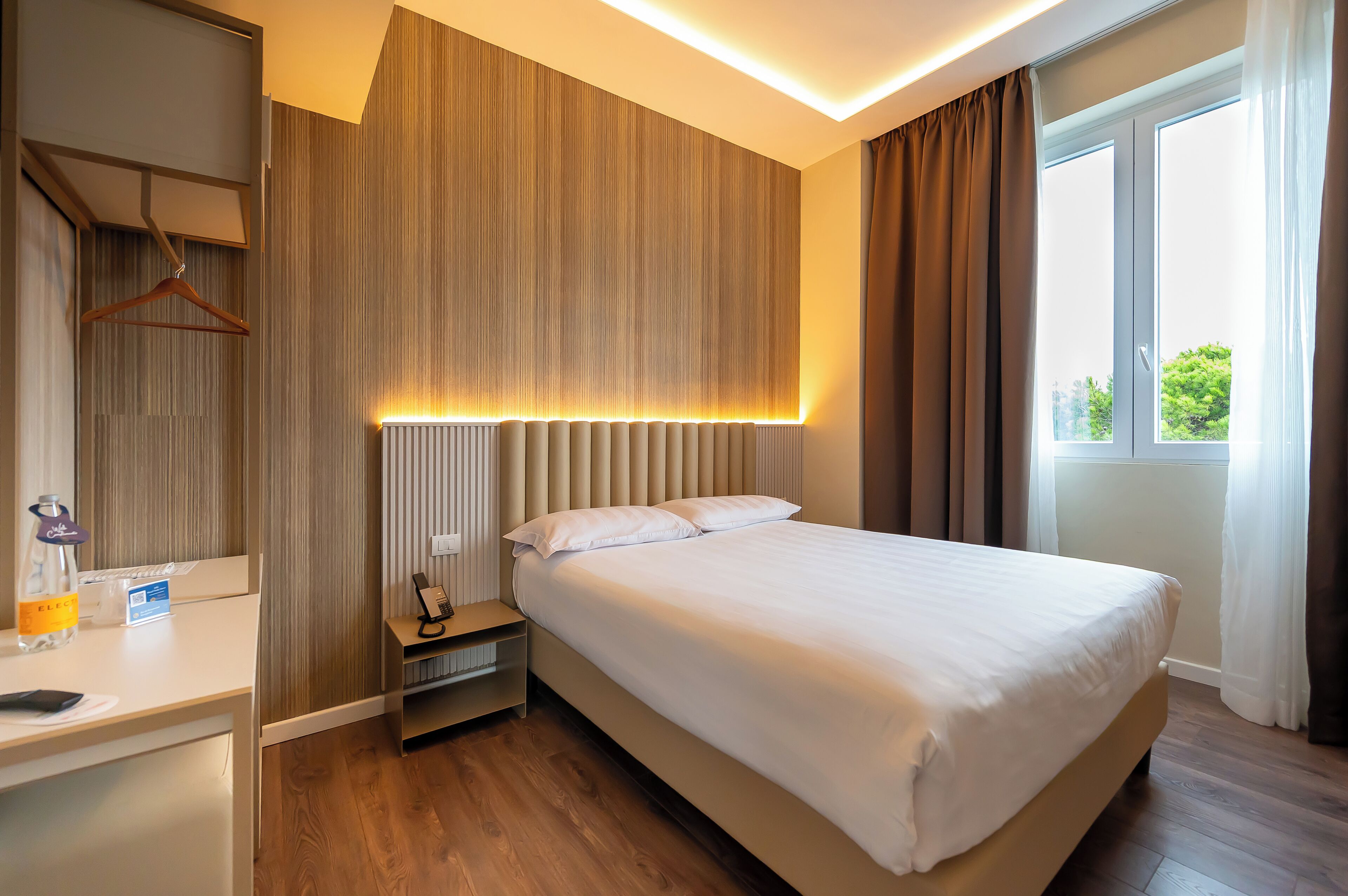 A hotel room with a bed, bedside table, and a window with curtains.