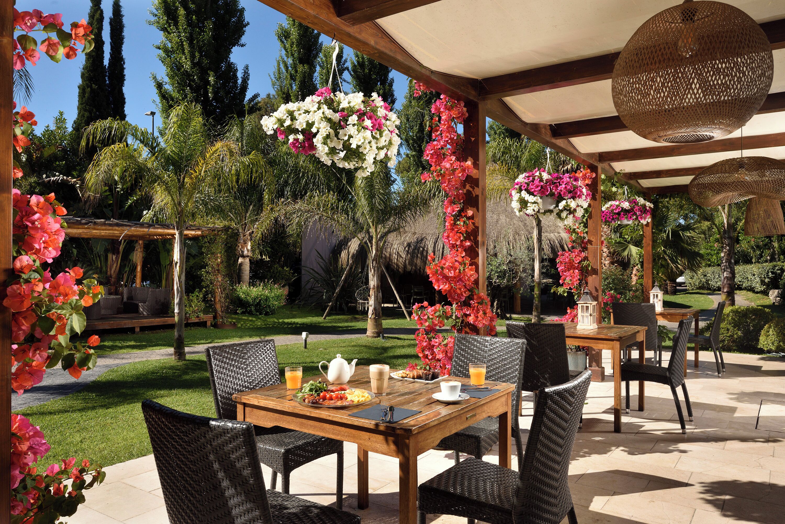 An outdoor patio with wicker furniture, a wooden table, and hanging flower arrangements.