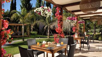 An outdoor patio with wicker furniture, a wooden table, and hanging flower arrangements.