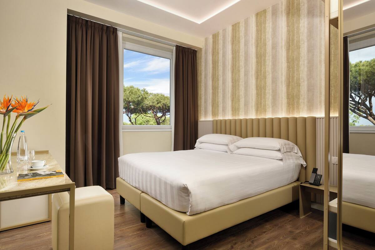 Una habitación de hotel con cama, mesita de noche y vistas a árboles.