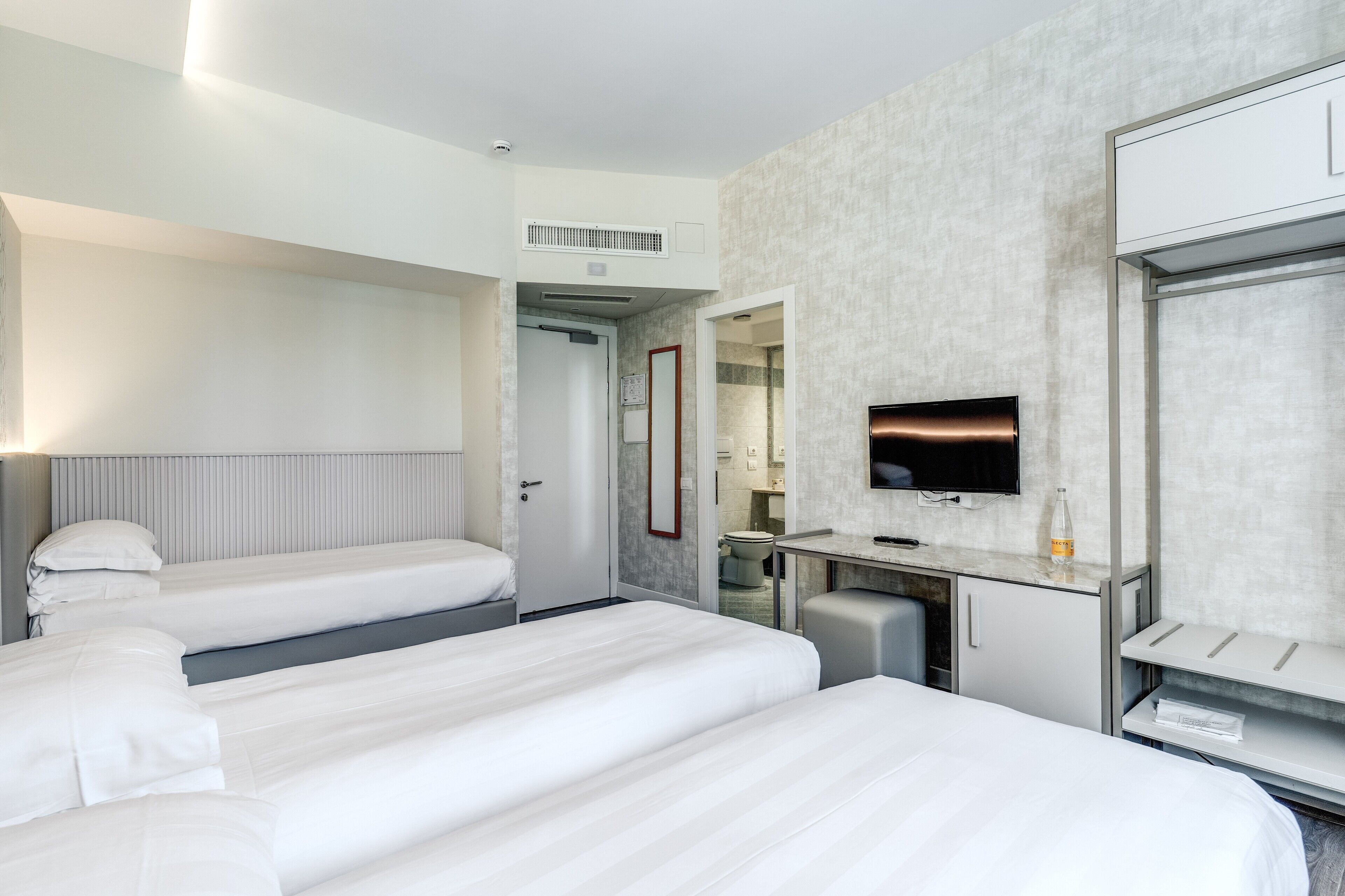 A hotel room with two beds, a desk, a TV, and a bathroom visible through an open door.