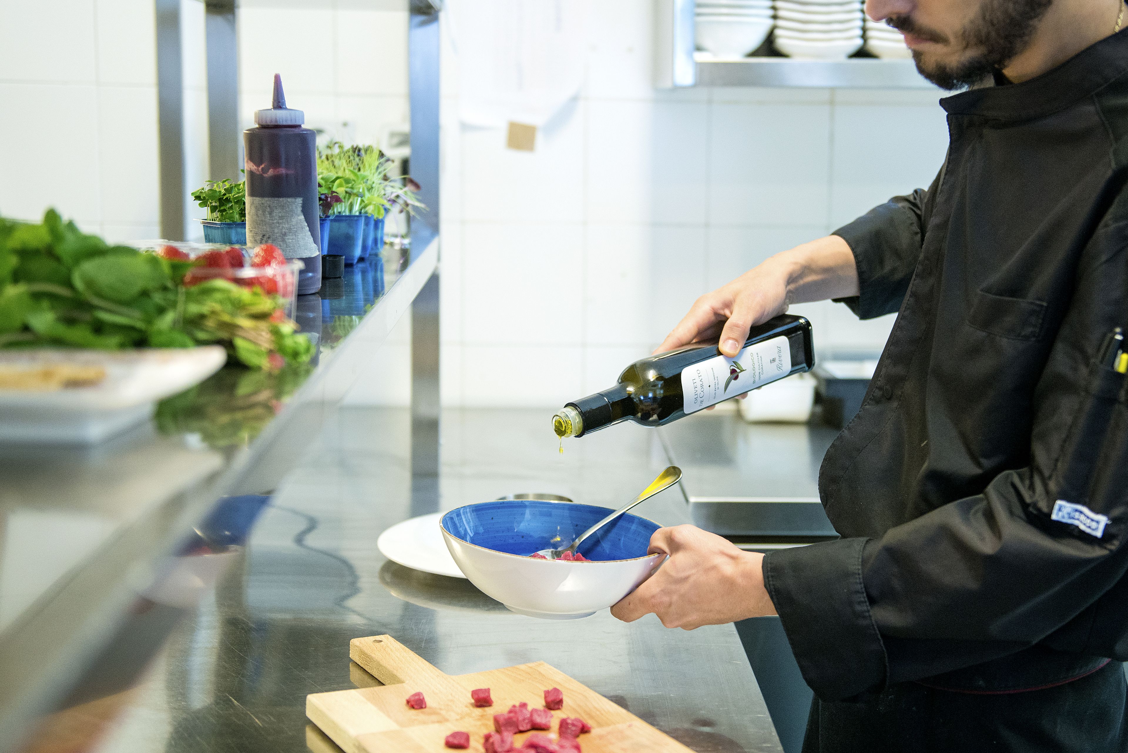 A chef pouring olive oil into a bowl with a spoon.