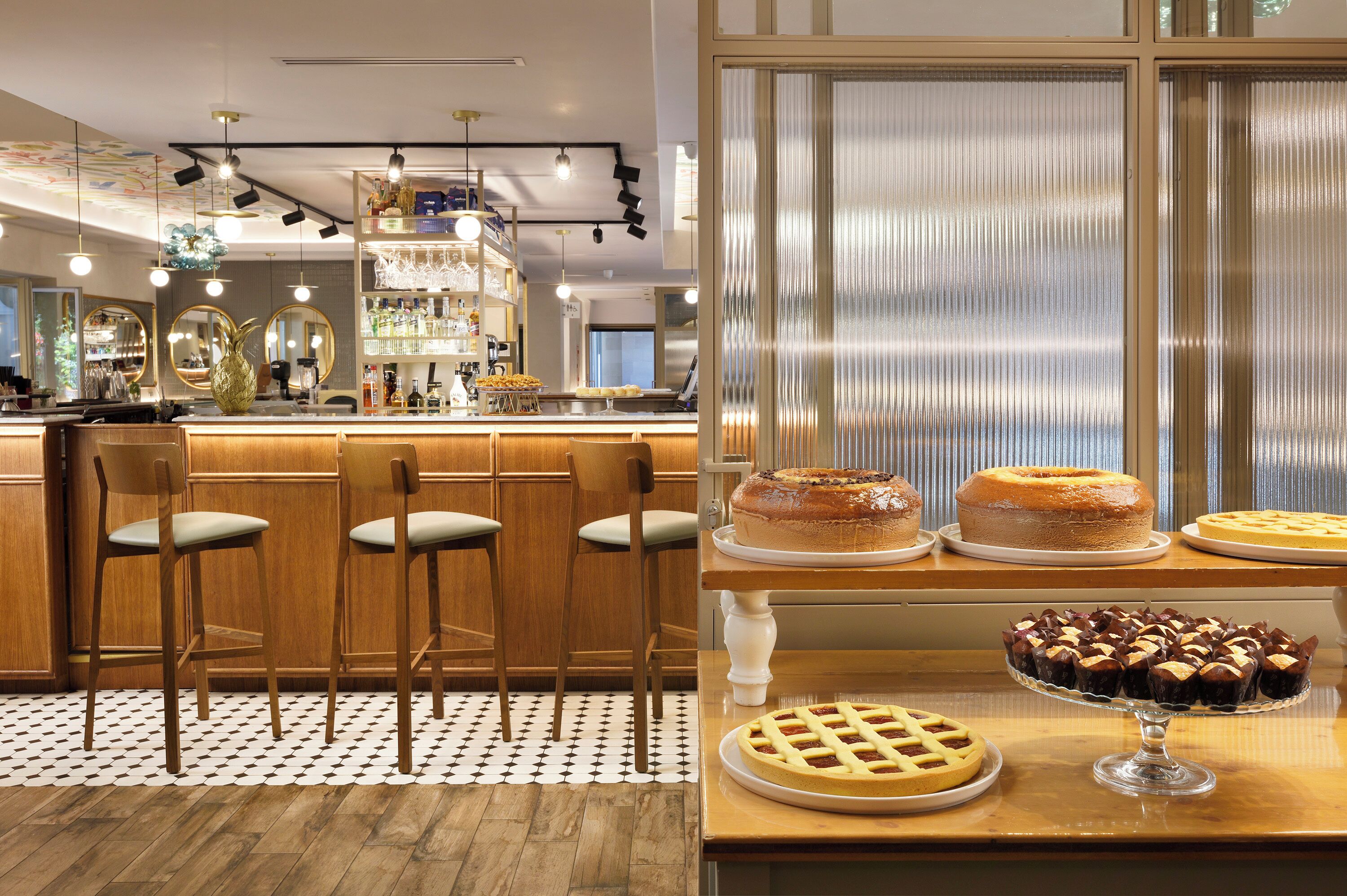 A bar area with wooden chairs, a counter with bottles, and a display of cakes and pies.