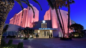 A hotel with a curved facade, palm trees, and a sign reading 'ISOLA SACRA.'