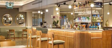 A bar area with wooden bar stools, a counter with bottles and glasses, and a decorative ceiling.