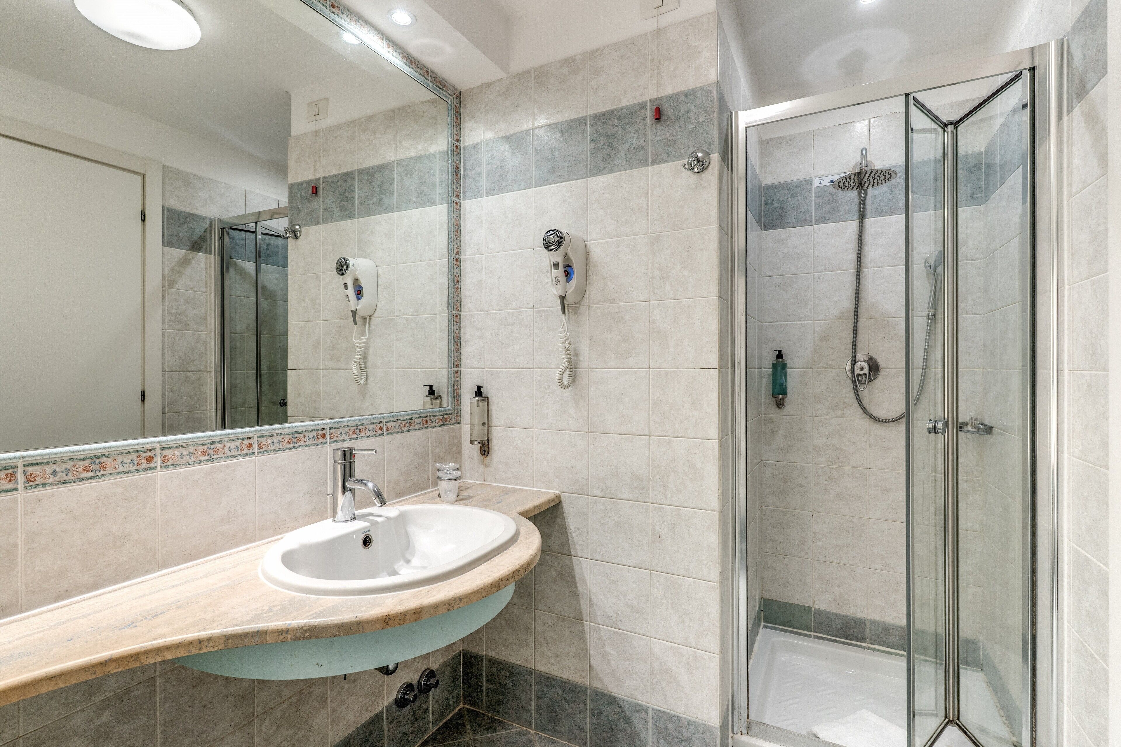 Un baño moderno con ducha envuelta en vidrio, un lavabo con encimera de mármol y un espejo con marco decorativo.