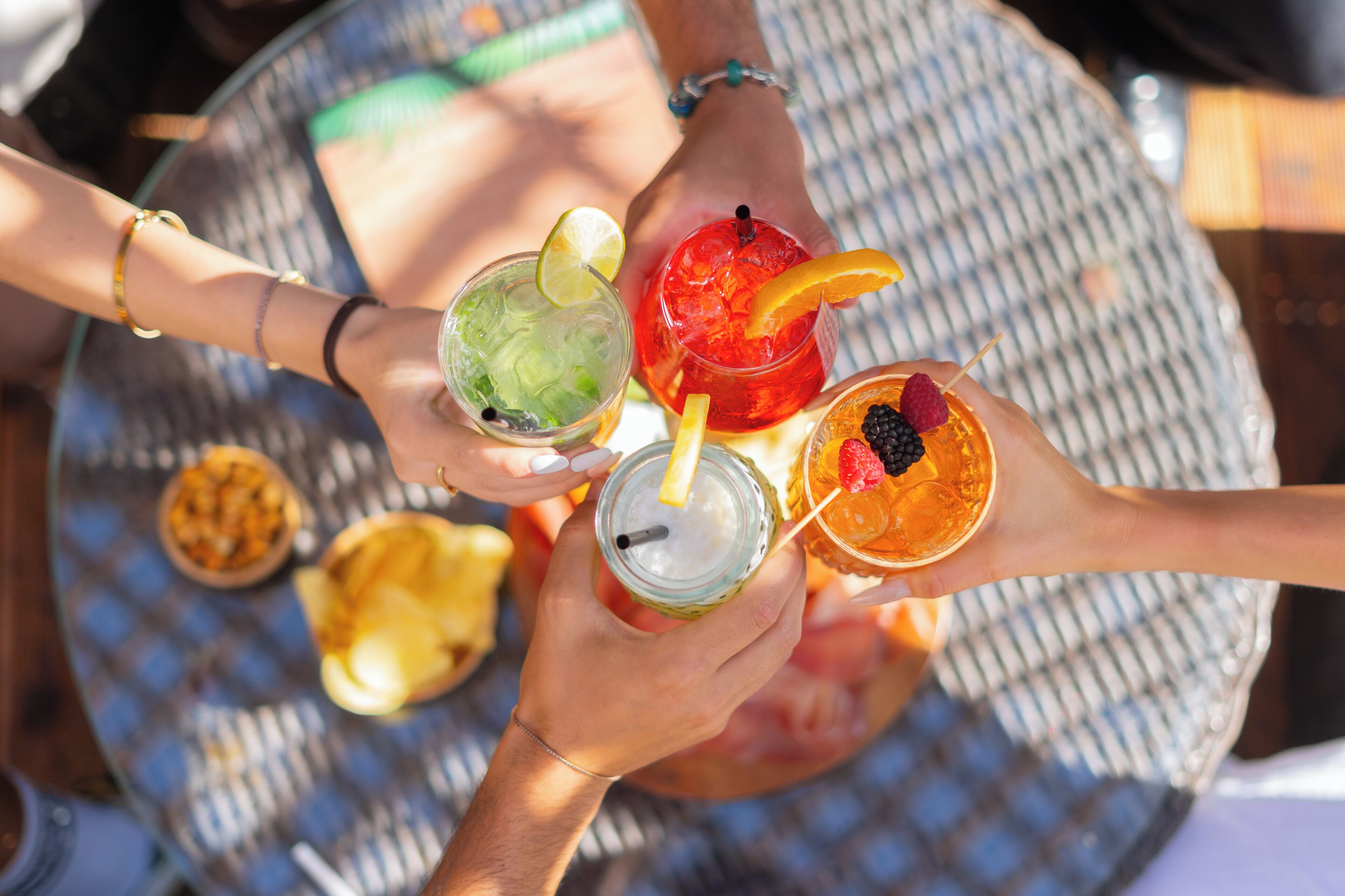 A group of people holding drinks with various garnishes, a checkered tablecloth, and a bowl of nuts in the background.