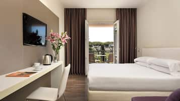 Habitación de hotel con cama, escritorio con silla, televisor montado en la pared y ventana con cortinas.