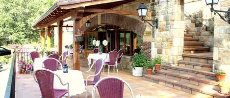 An outdoor patio area with wicker chairs and tables, stone steps, and potted plants.