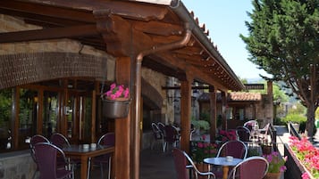 An outdoor café area with wooden tables and chairs, a hanging flower pot, and a sign reading "Restaurant".
