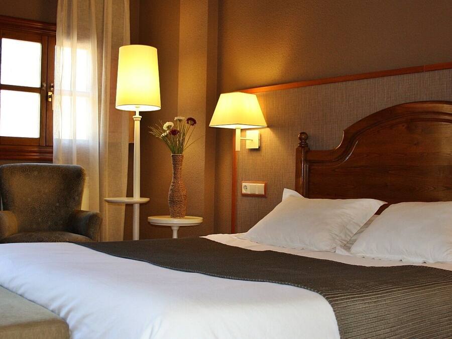 Habitación de hotel con una cama grande, dos lámparas de noche, una silla y una mesita con un florero.