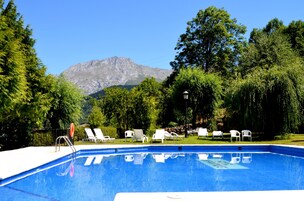 Una piscina con sillas de descanso blancas y una montaña al fondo.