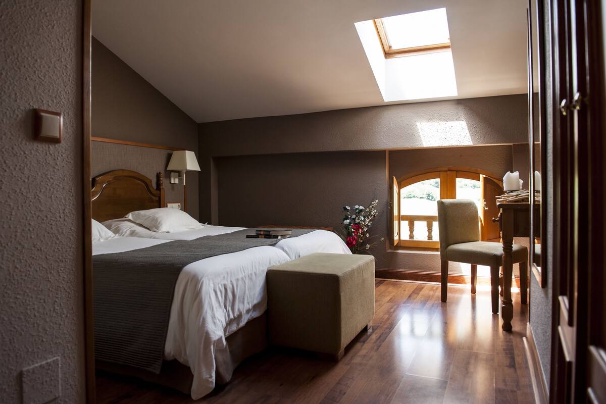 Une chambre à coucher avec un lit, une table de chevet, une lampe et une vue sur l’extérieur.