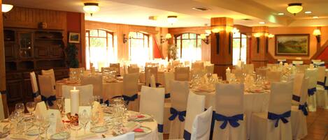 A banquet hall with round tables set for a formal event, featuring white tablecloths and blue chair sashes.