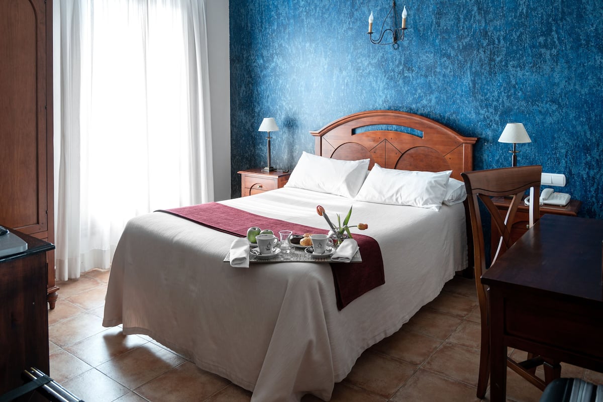 Un lit bien fait, avec un plateau de petit-déjeuner, une tête de lit en bois et un mur bleu à la texture intéressante.
