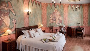 A spacious bedroom with a large bed, a desk, and a chair. There are wall murals and a chandelier. - Hotel El Jardín de la Abadía (Arroyo de la Encomienda)