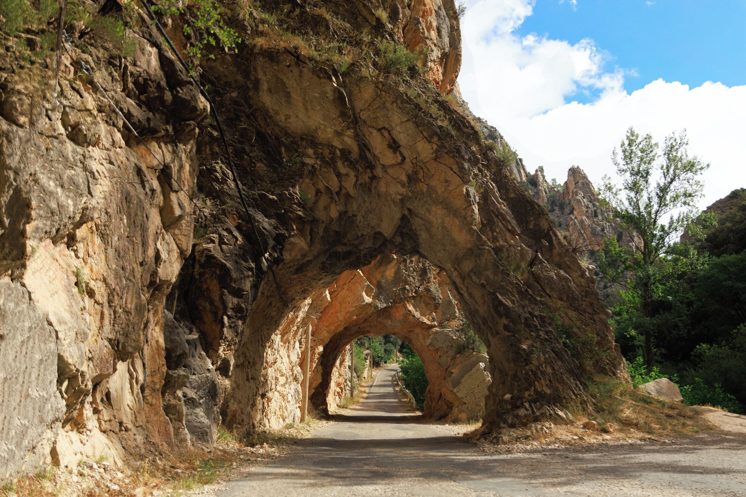A natural rock archway over a dirt road with greenery on either side.