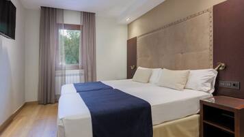 A hotel room with a large bed, a bedside table, a window with curtains, and a ceiling fan.
