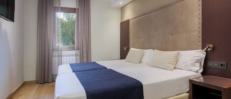 A hotel room with a large bed, a bedside table, a window with curtains, and a ceiling fan.