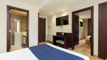 A hotel room with a bed, a desk, a television, and a bathroom visible through an open door.