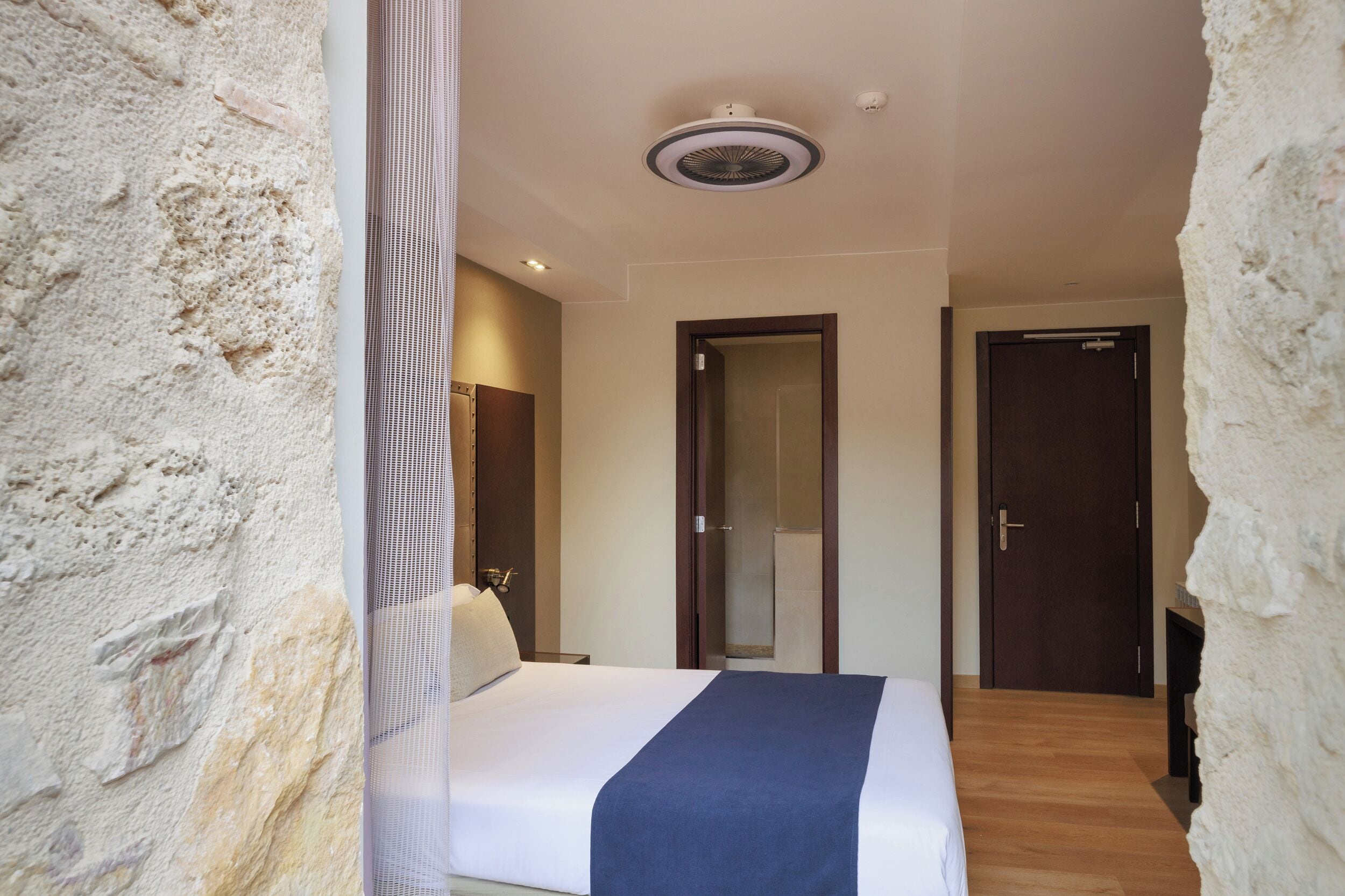 Una habitación de hotel con una cama, una puerta y una lámpara en el techo.
