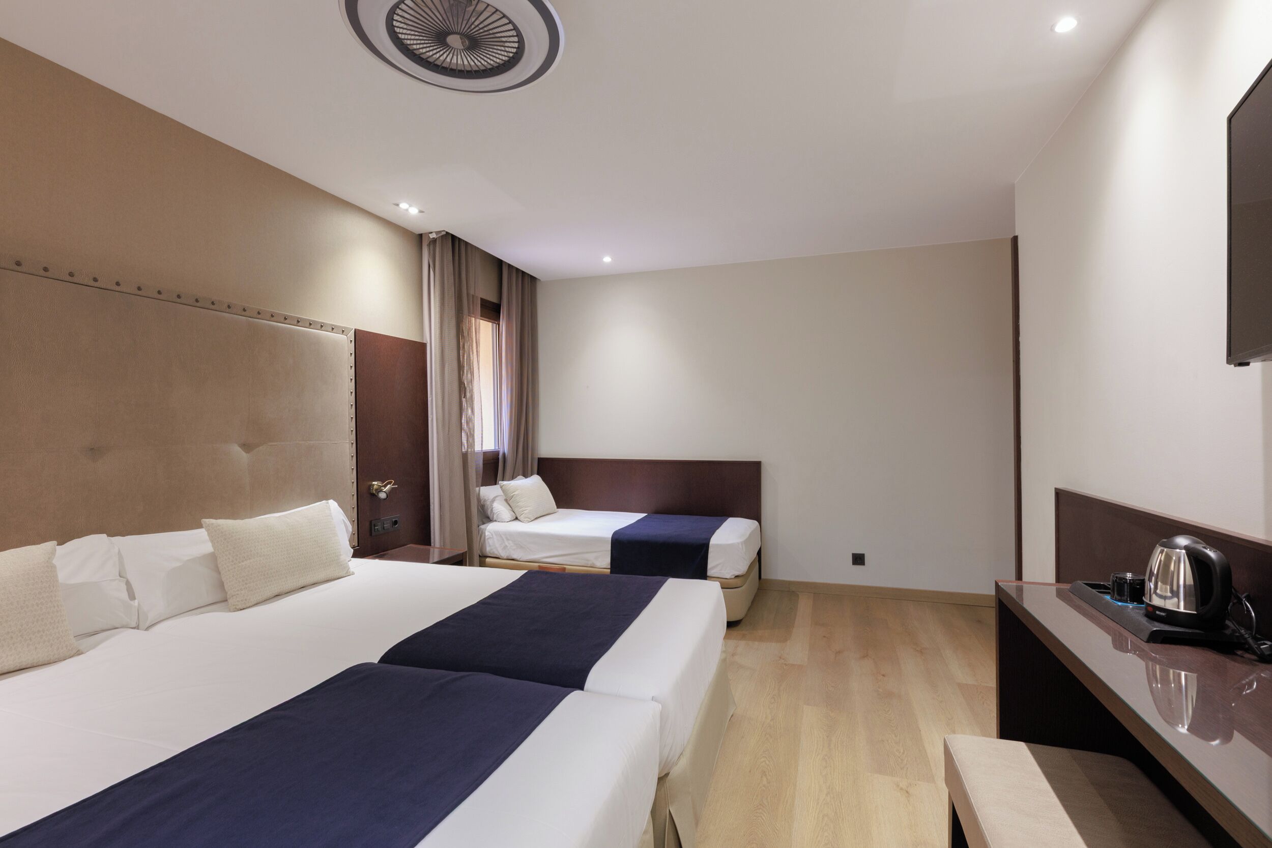 A hotel room with two beds, a desk with a coffee maker, and a wall-mounted TV.