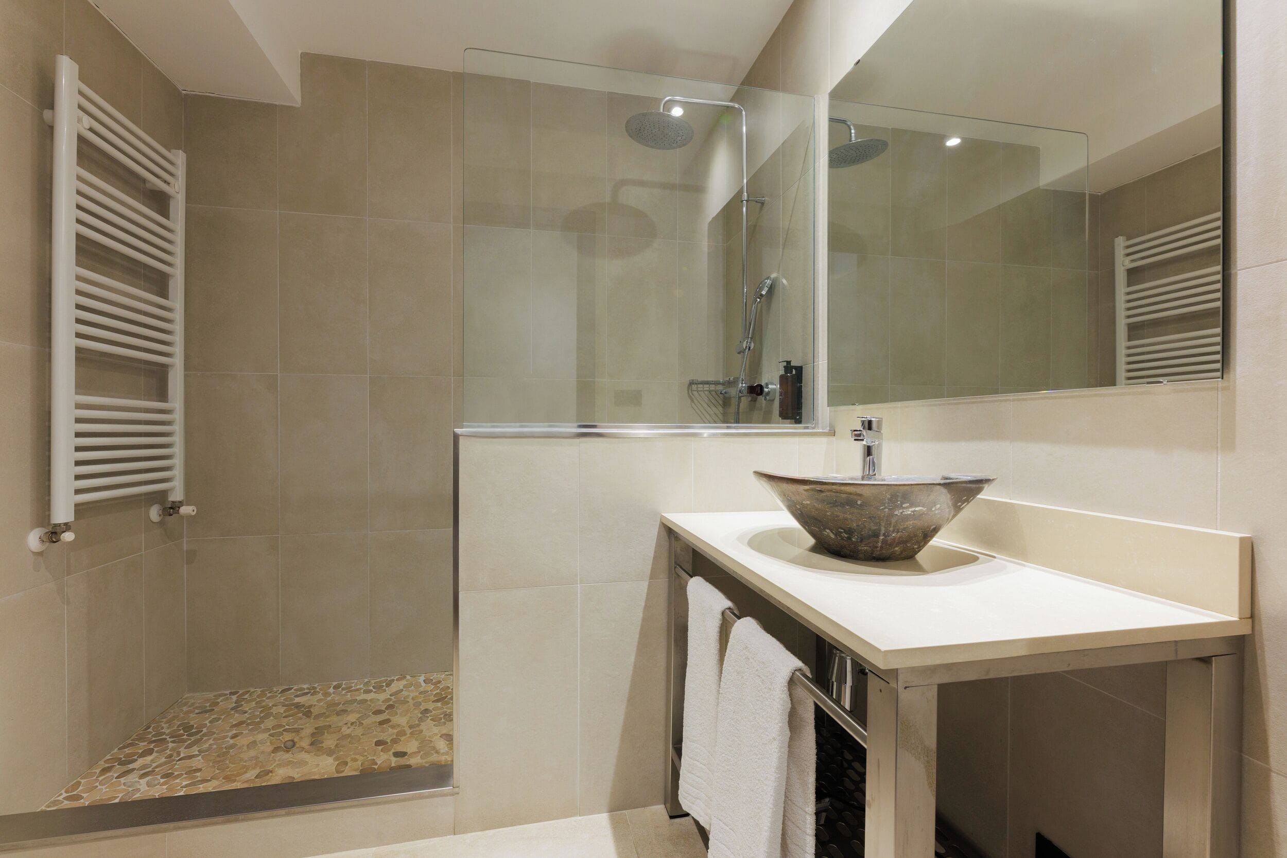 A modern bathroom with a glass-enclosed shower, a large mirror, and a stone basin sink.
