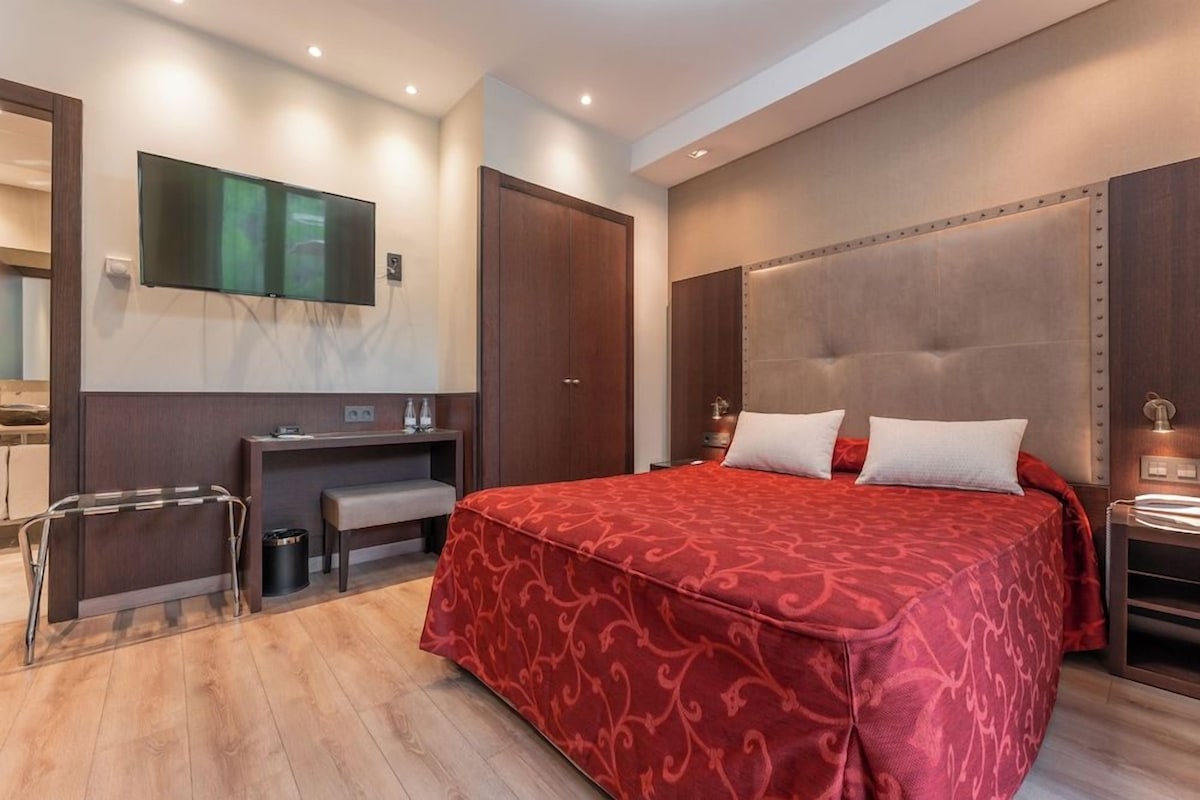 Habitación de hotel moderna con una cama grande, un escritorio con silla, un televisor montado en la pared y un armario.