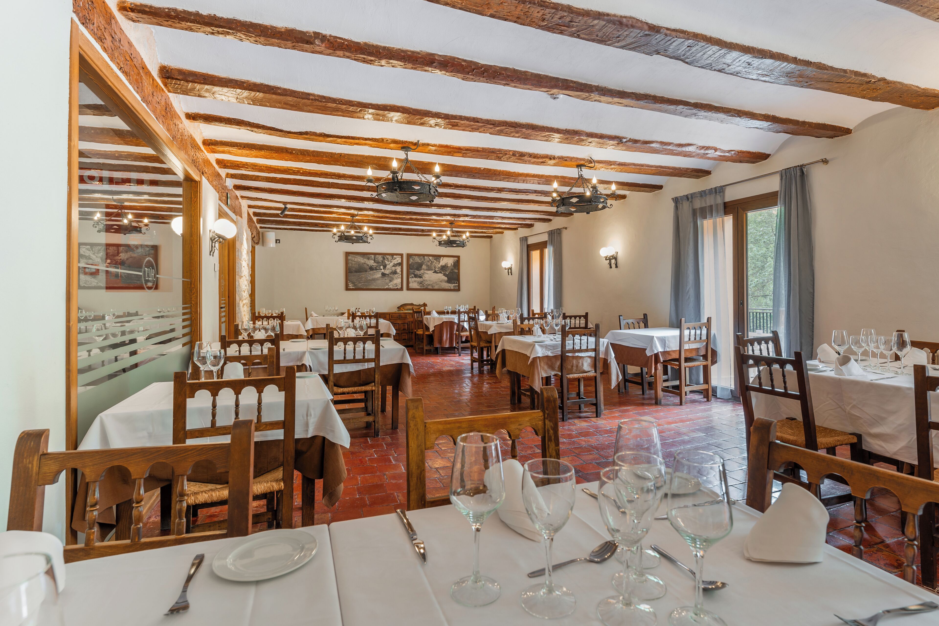 Un restaurante con vigas de madera, mesas y sillas blancas, y piso de ladrillo rojo.