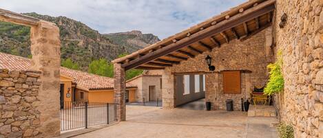 A courtyard with stone buildings, a wooden pergola, and a mountain backdrop.