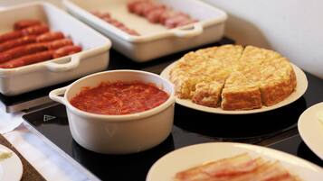 A table with various food items including a dish of sliced meat, a bowl of red sauce, and a round baked item.