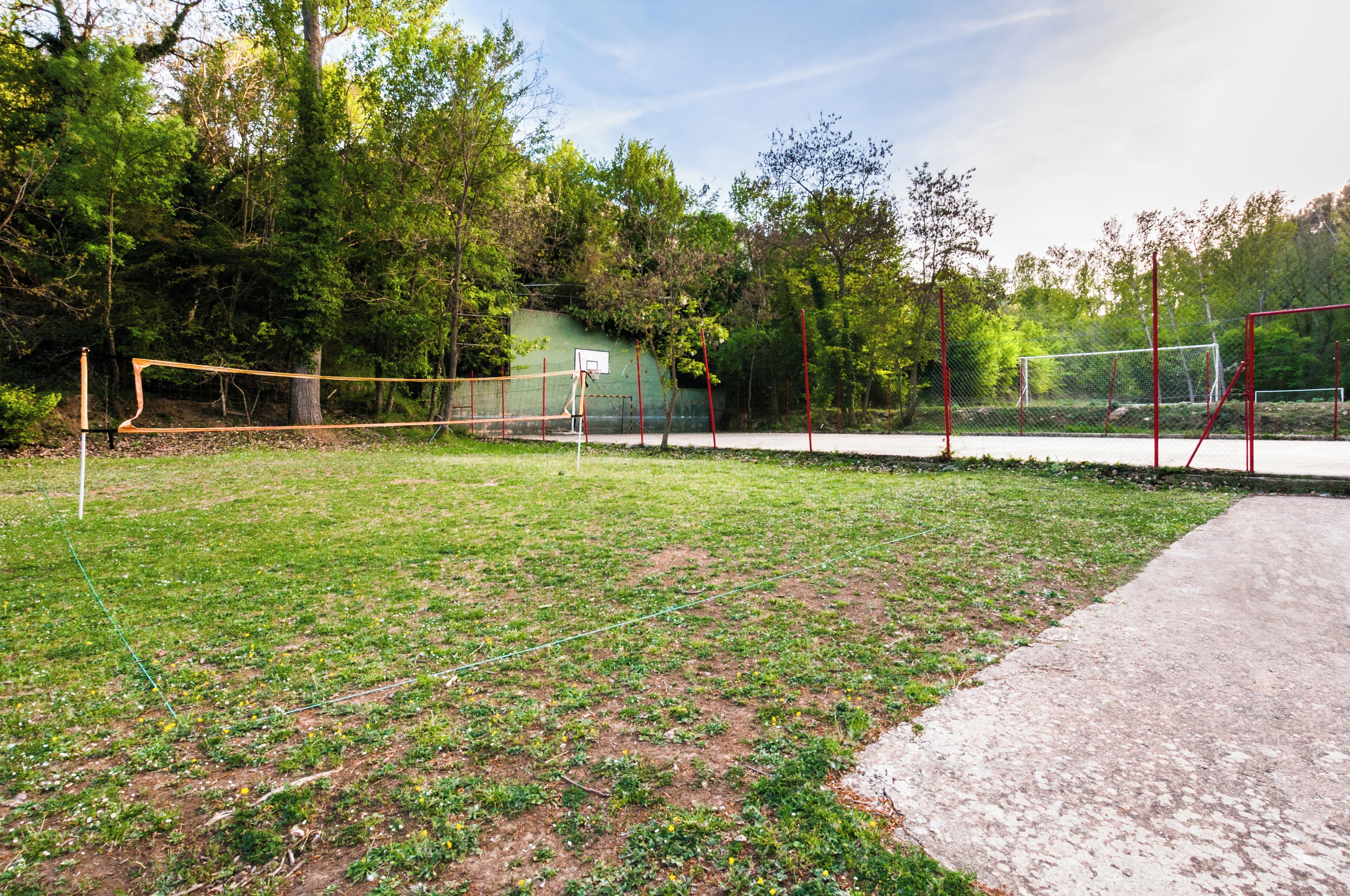 A tennis court with a net, surrounded by a grassy area and trees.