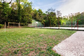 Una cancha de tenis con una red, rodeada de césped y árboles.